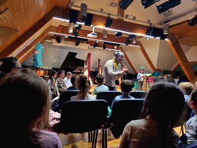 Glasbena pravljica v glasbeni šoli – igralka v vlogi miške, igra na blok flavto, v ospredju otroci